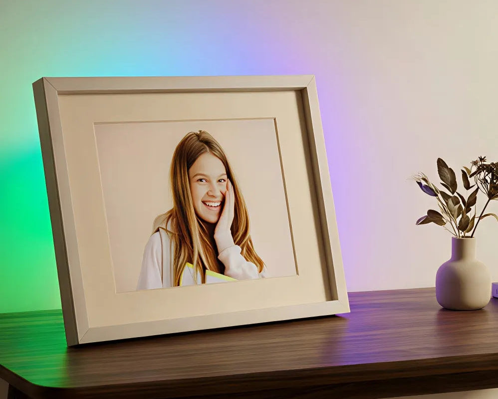 iFramix smart frame with an integrated colorful LED light strip creating a soft breathing glow on the wall behind a portrait photo.